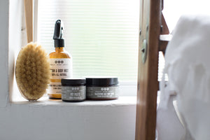 scrub brush with room & body mist, pit paste and salt scrub by Really Great Goods, on windowsill with ladder and towel